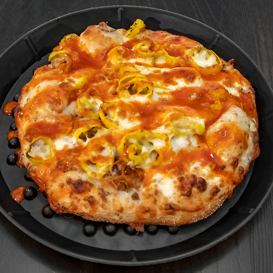 A round pizza with melted cheese, red sauce, and yellow banana peppers on a black pan.