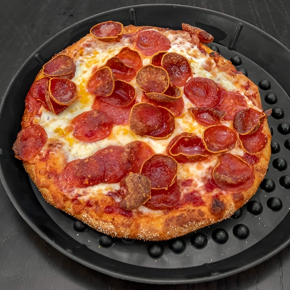 A small, round pepperoni pizza with a crispy crust sits on a black pizza pan.