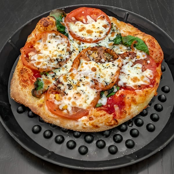 A freshly baked pizza with melted cheese, tomato slices, and basil on a dark, textured pan.